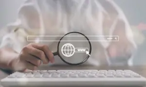 Dłoń z lupą bada ikonę globu i "www" podświetloną na tle paska wyszukiwania. Kluczowe dla **techniczne seo**.